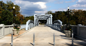 A brand-new bridge painted light blue a with new paved road, potted plants on the side, and a sidewalk.