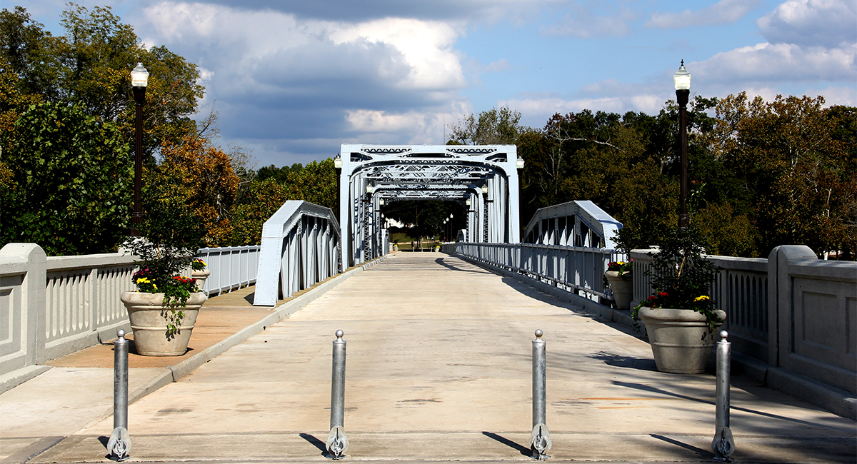 A brand-new bridge painted light blue a with new paved road, potted plants on the side, and a sidewalk.