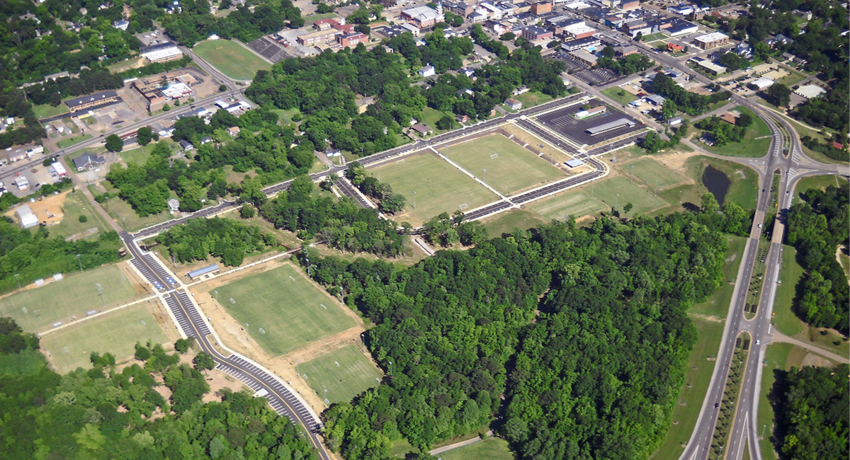An aerial view of a park where a series of soccer fields surrounded by wooded areas.