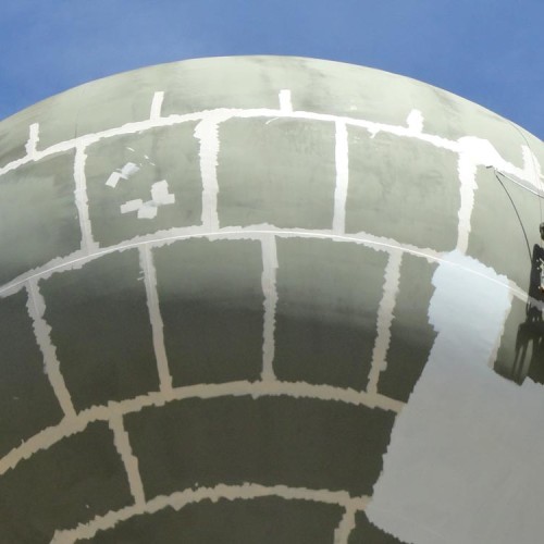 Two people painting the dome of a water tower.