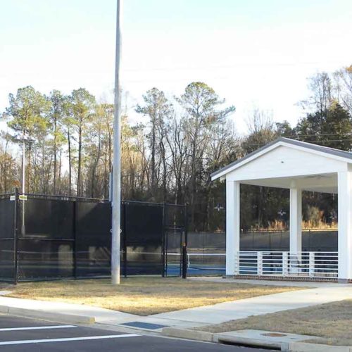 The Brandon Tennis facility, surrounded by fence, and with a white covered pavillion on the side.