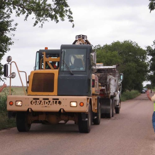 Two construction workers directing an excavator on an unpaved road.