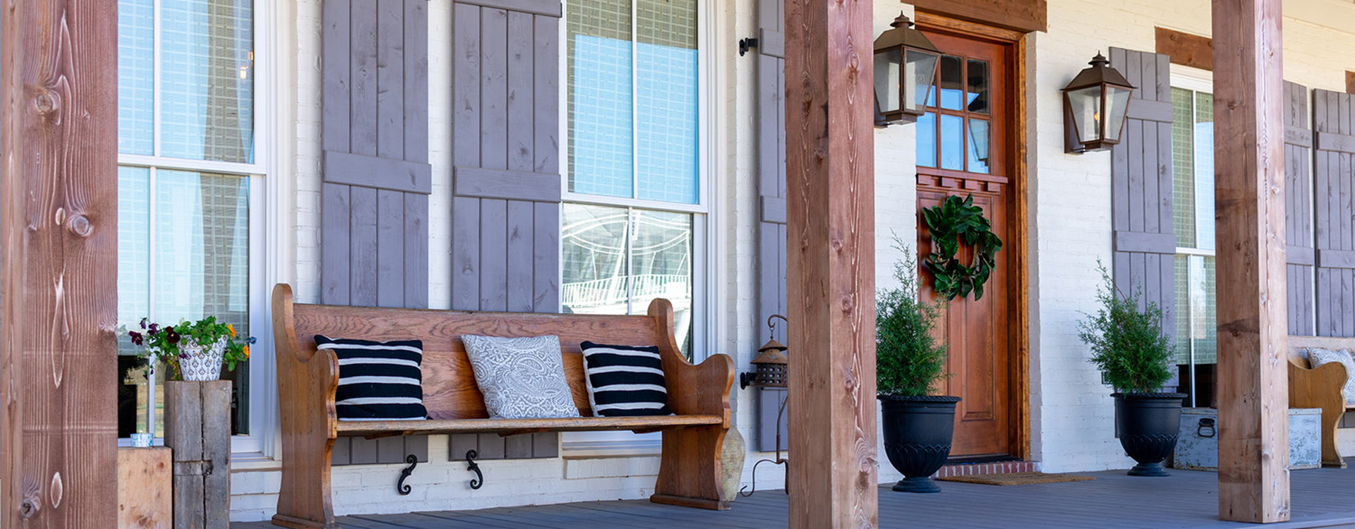 A front porch with a wooden bench covered in throw pillows.