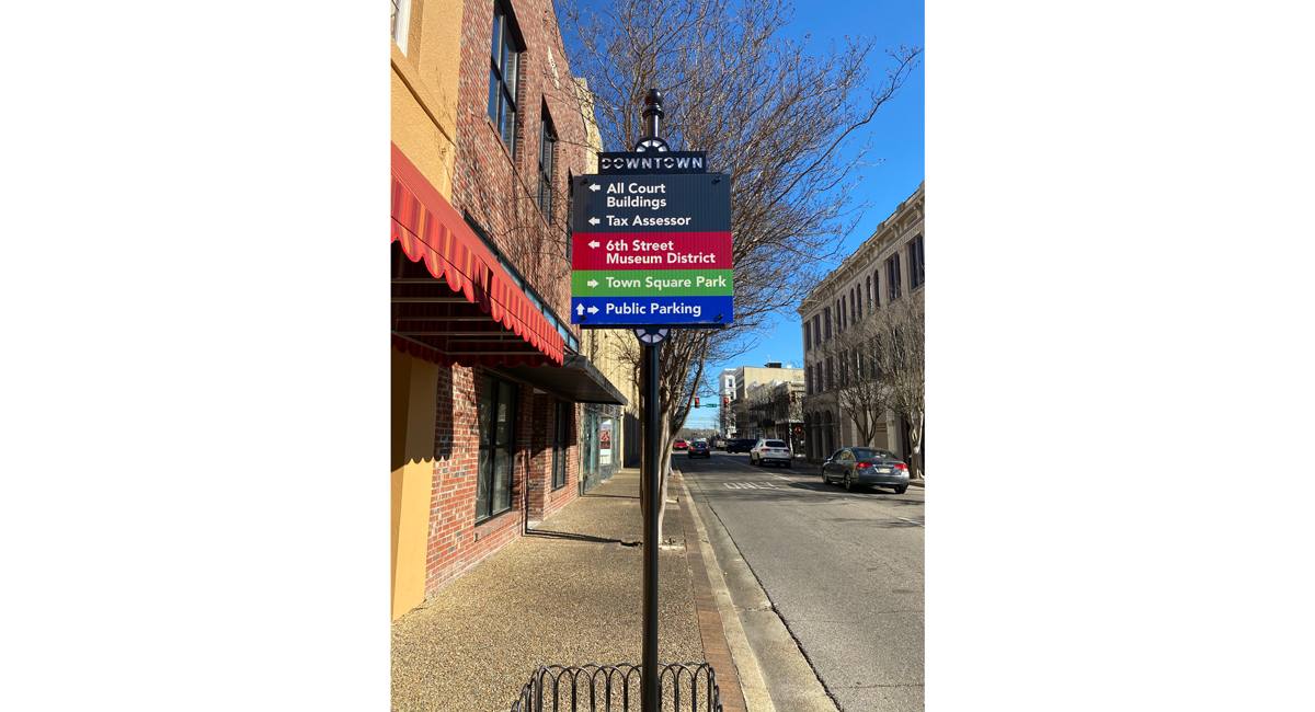 A sign on a sidewalk that points directions to "All Court Buildings," "6th Street Museum District," "Town Square Park," and "Public Parking."