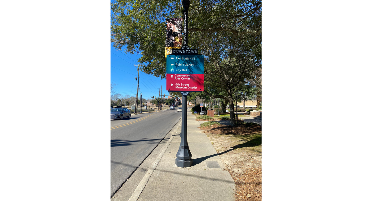 A sign on a lamp post that gives directions to "Fire Station #1," "Public Library," "City Hall," "Community Arts Center," "6th Street Museum District."