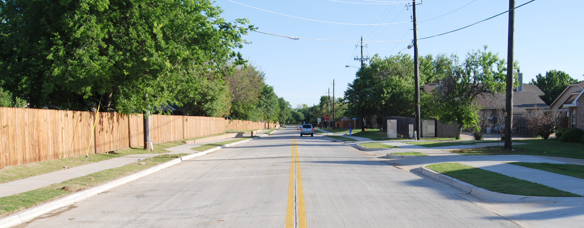 A suburban street with a fence on one side and houses on the other.
