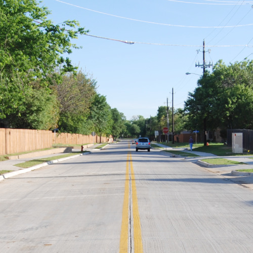 A suburban street with a fence on one side and houses on the other.