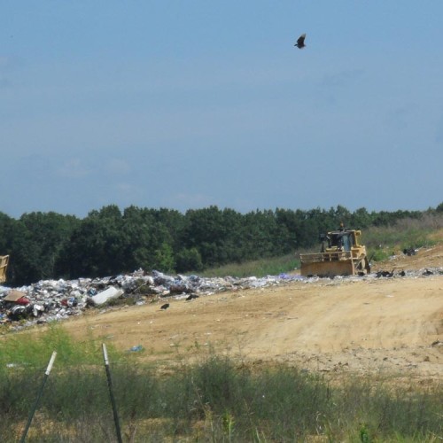 Bulldozers working on a sandy area with trash off to the side.