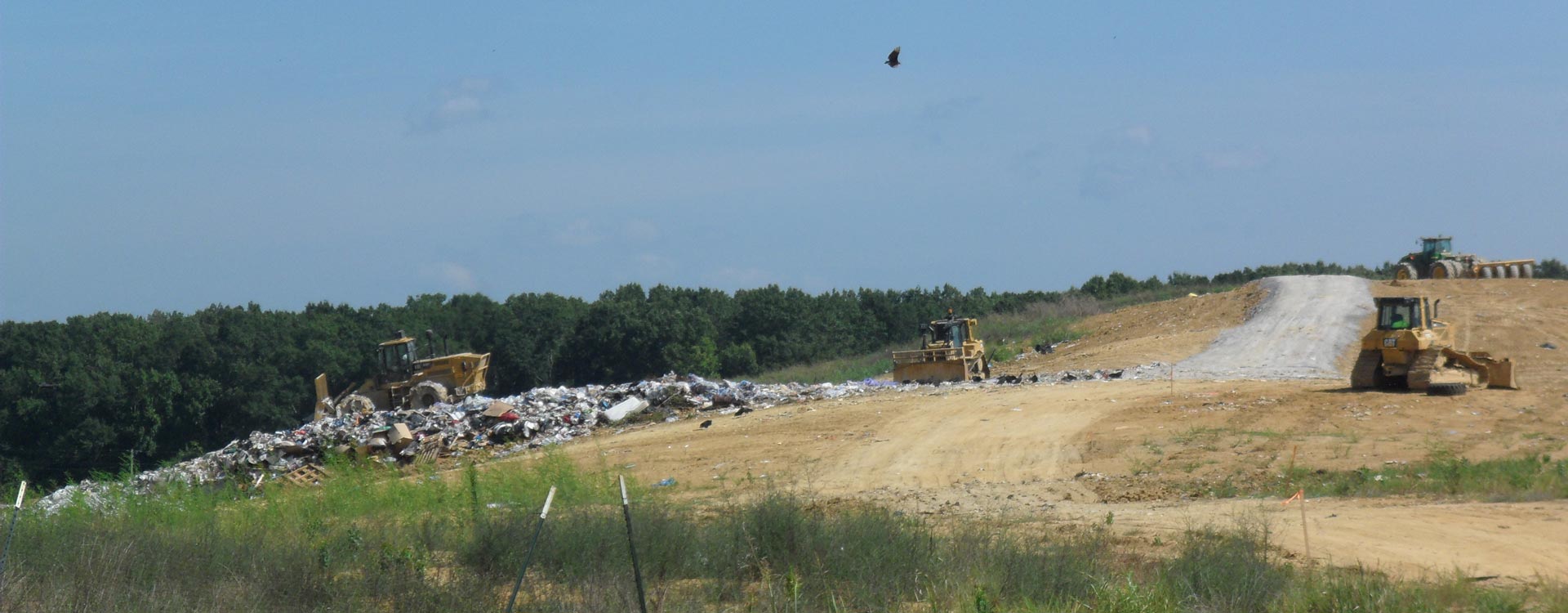 Bulldozers working on a sandy area with trash off to the side.